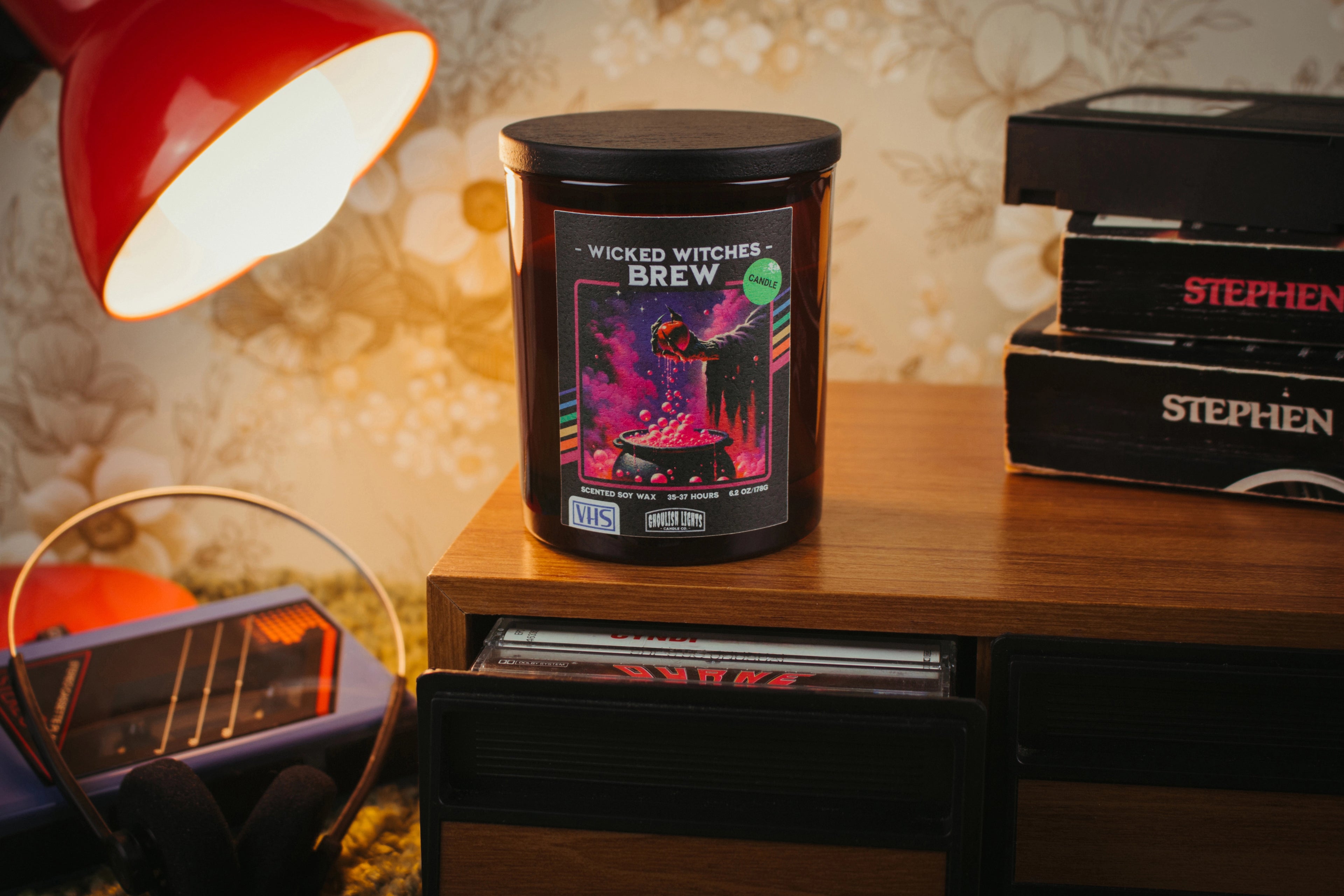 Handgemachte 80er-Horror-Kerze im VHS-Kassetten-Design auf Nussbaumholz-Deck vor vintage 80er-Jahre-Blumentapete