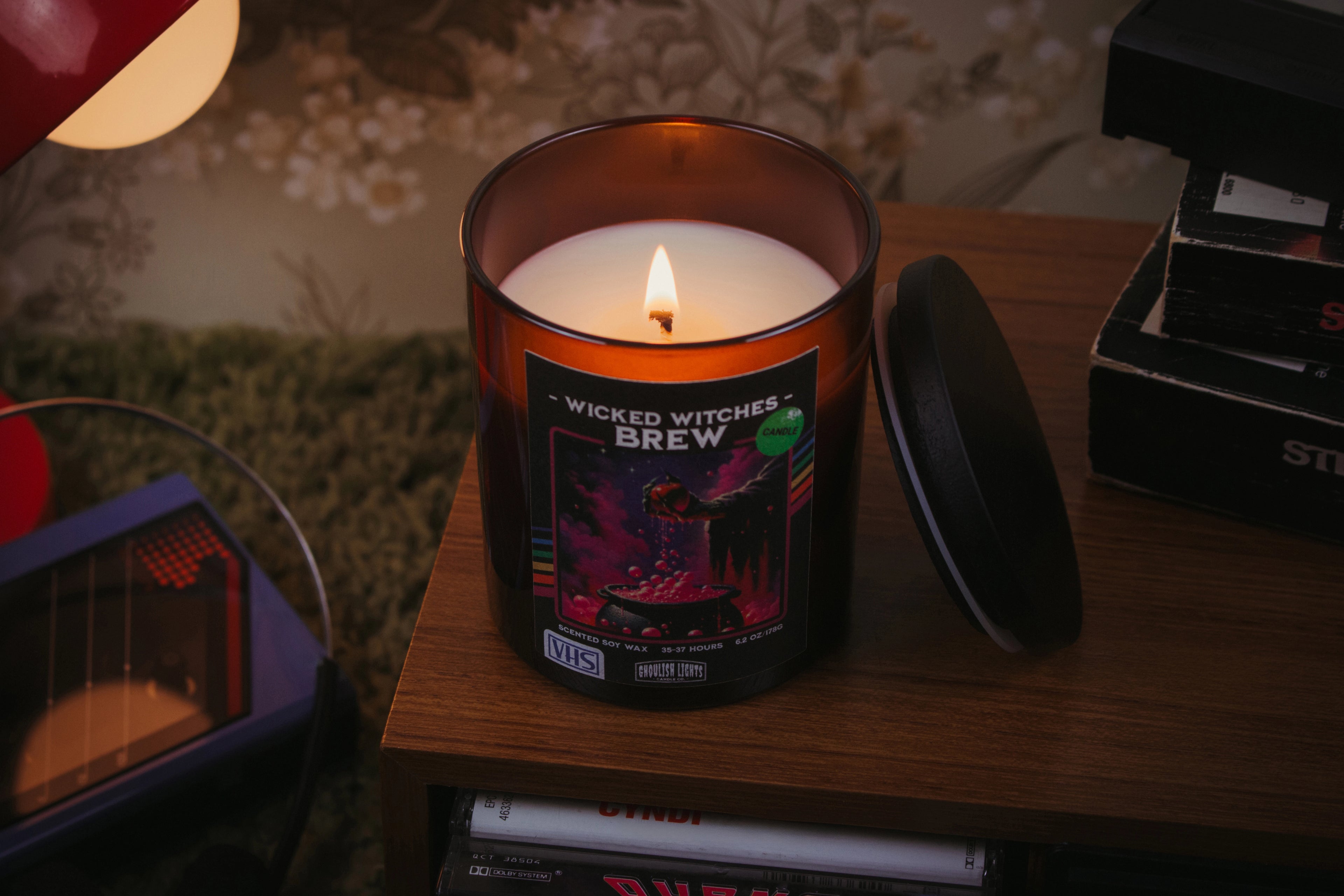 Handgemachte 80er-Horror-Kerze im VHS-Kassetten-Design auf Nussbaumholz-Deck vor vintage 80er-Jahre-Blumentapete