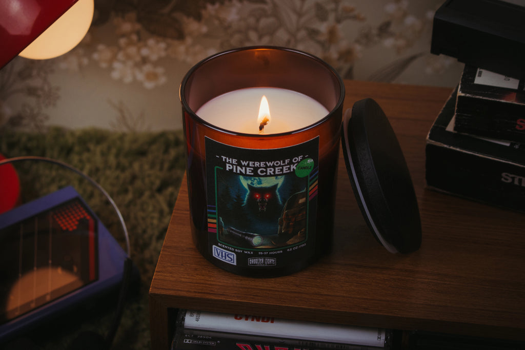 Handgemachte 80er-Horror-Kerze im VHS-Kassetten-Design auf Nussbaumholz-Deck vor vintage 80er-Jahre-Blumentapete